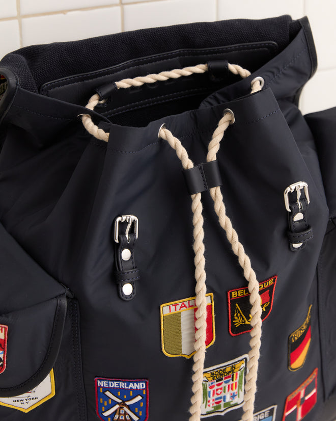 Close-up of the Interrail Rucksack, a black bag with rope drawstrings and vibrant embroidered country patches—an eye-catching accessory for any adventure.