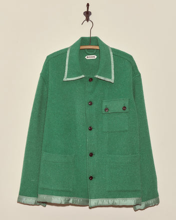 The Island Mists Jacket - L features green wool with contrasting light green trim, front buttons, three pockets, and a collar. Made in New York, this unique jacket hangs elegantly on a hook.