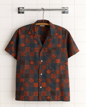 The Jaipur Geometric Shirt - M/L features short sleeves and a red and dark blue geometric print, crafted from deadstock fabric for a unique look. Shown hanging on a hanger.