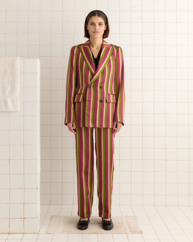A person in a Juniper Stripe Double-Breasted Suit Jacket stands in a tiled room, where the elegance of Kutnu fabric meets the practicality of a towel on the left wall.