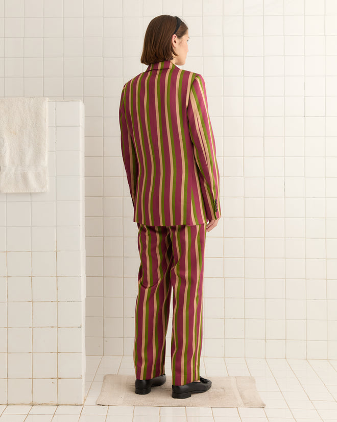 In a tiled room, a person with their back to the camera wears the Juniper Stripe Double-Breasted Suit Jacket, crafted from elegant Kutnu fabric.