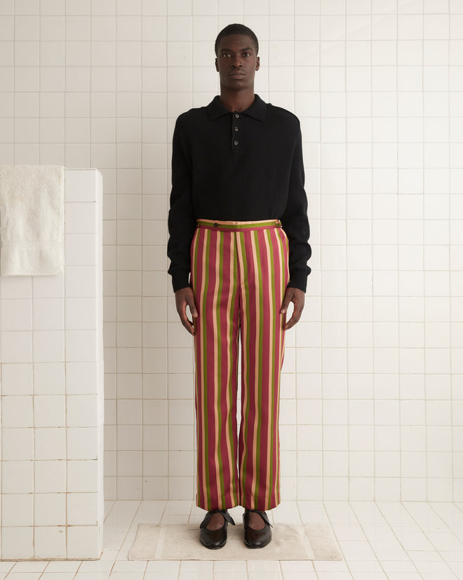 A person wearing a black long-sleeve shirt and the Juniper Stripe Trousers stands in a tiled room with white walls.