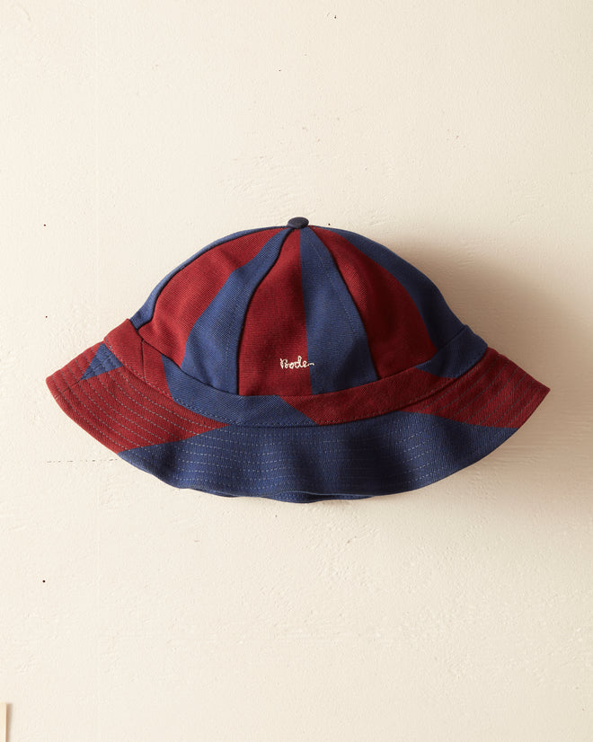 The Killington Stripe Hat, a red and blue bucket hat made from 100% cotton, features a small white embroidered Bode logo on the front and is displayed against a plain light-colored background.