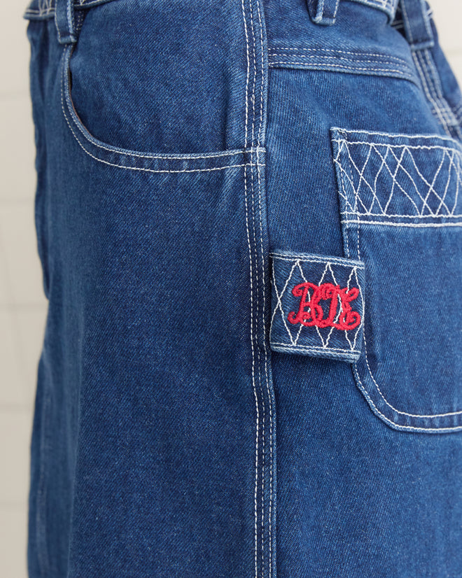 Close-up of blue denim fabric from the Embroidered Denim Skirt, featuring detailed white stitching, a quilted pocket design, and red embroidered initials reminiscent of a Bode piece.
