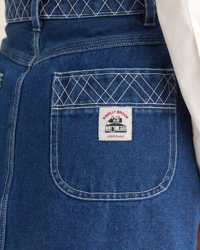 A close-up of the Embroidered Denim Skirt's pocket features white stitching and a "KNOLLY BROOK, a BODE product" label, showcasing craftsmanship and subtle elegance synonymous with timeless denim artistry.