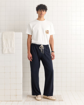 A man wearing navy Lace-Front Sweatpants and a white T-shirt stands facing forward in a white-tiled bathroom.