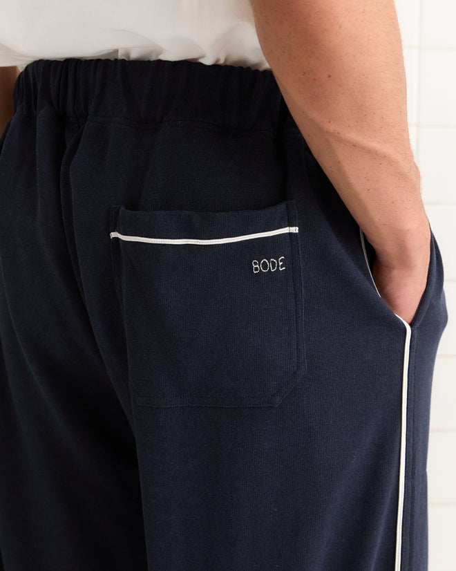 Close-up of a person wearing Lace-Front Sweatpants in navy heavyweight fabric, featuring a white trim and "BODE" embroidered on the back pocket.