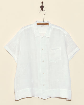 The Lacework Sample Short Sleeve Shirt (XL) is a white handmade button-up with a chest pocket, displayed on a wooden hanger against a beige wall.