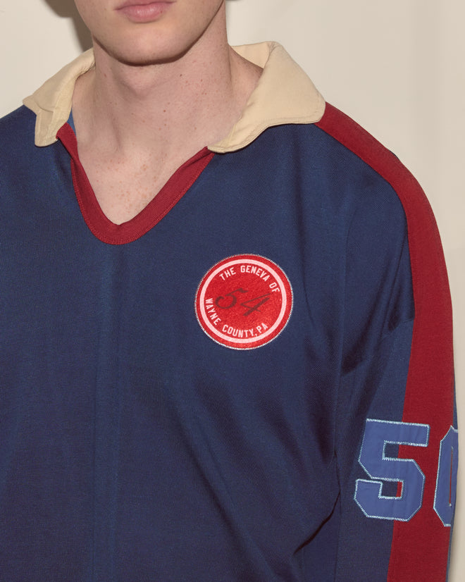 Wearing the Lakewood Polo—a blue rugby shirt with a red badge, number 50 on the sleeve, and a beige collar—makes it perfect for summer camp.