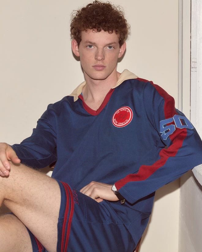 Young man with curly hair sits indoors, looking directly at the camera while wearing the Lakewood Polo.