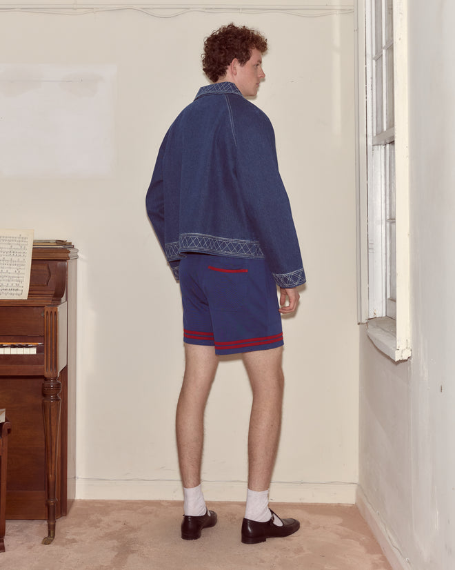 A person wearing Lakewood Shorts and a denim jacket stands indoors near a window, facing away from the camera.