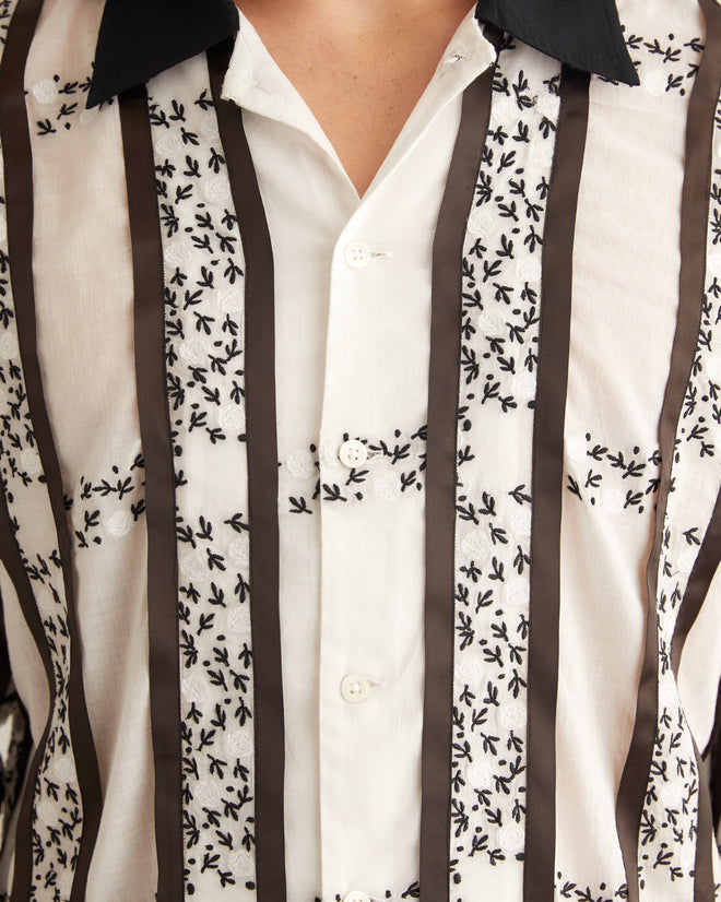 Black and white cotton shirt with black-and-white embroidered roses and stripes of satin ribbon. The shirt has a contrast collar and hem and an unfitted silhouette.