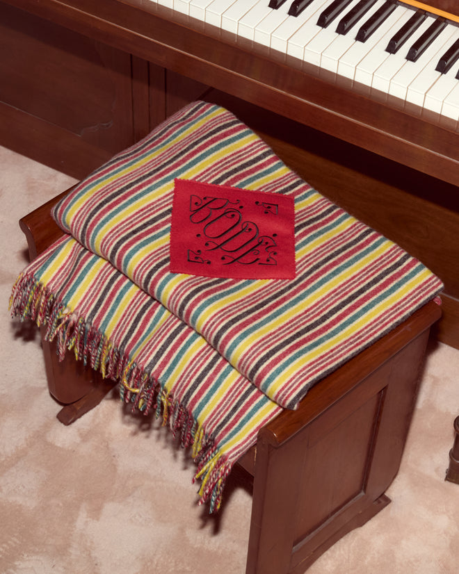 A Lawrence Throw Blanket and a red "LOVE" card rest on a wooden piano bench near a keyboard.