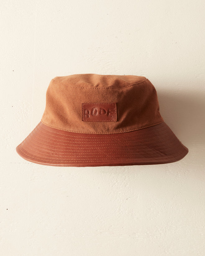 The Leather Brim Bucket Hat - Tan/Brown features a leather brim and a stitched label reading 