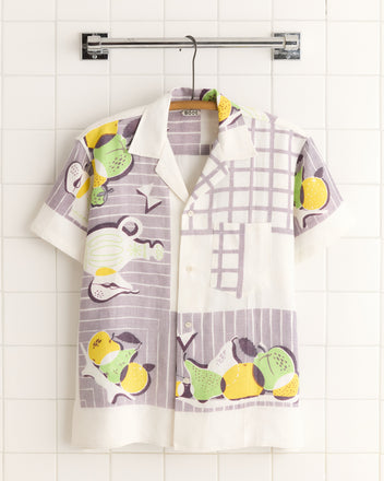 The Lemon Tree Shirt (M/L) features a vibrant fruit and midcentury kitchen print. Displayed on a hanger against white tiles, it exudes unique, one-of-a-kind charm.