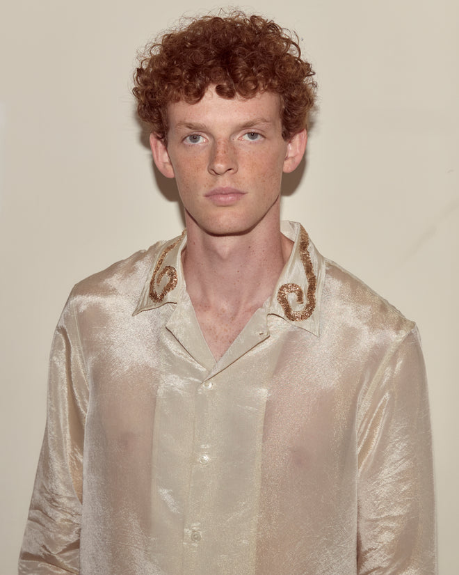 A young man with curly red hair wears the Lido Long Sleeve, a shiny cream-colored lamé shirt, standing against a plain background.