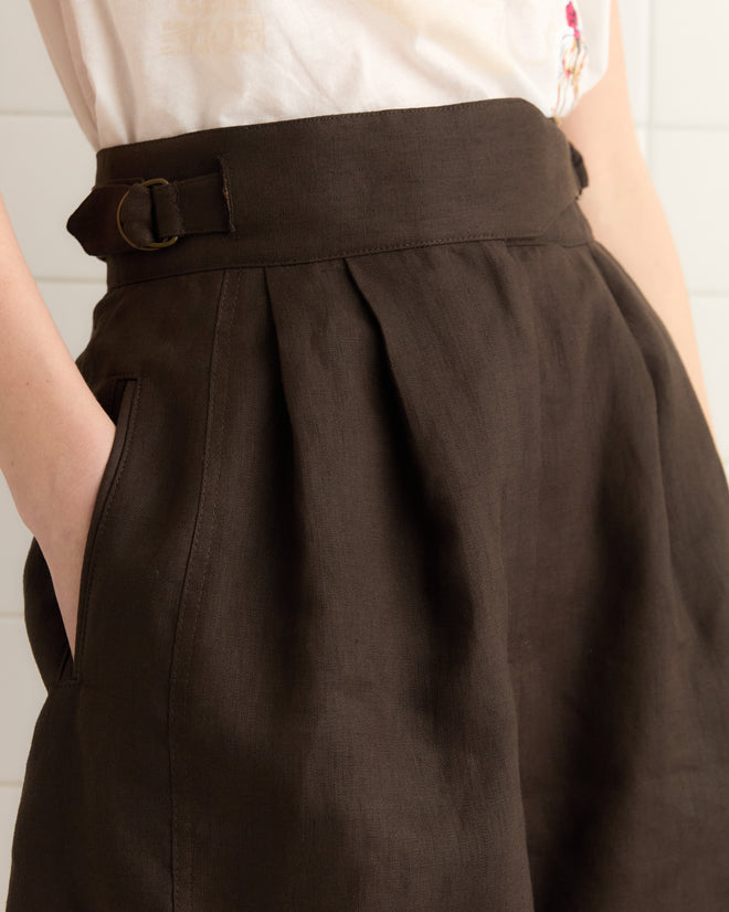 The individual is wearing the Linen Smith Shorts in brown/black, hands in pockets, exuding a touch of historical reproduction chic.