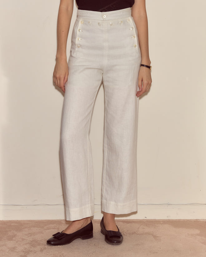 Person wearing 1940s-inspired Linen Sailor Trousers - White, paired with a black top and black loafers, standing against a plain wall.