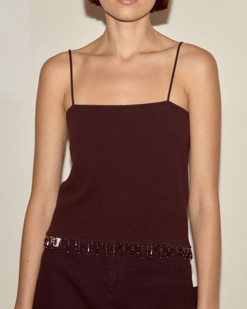 A woman wears the Lodge Tank in dark brown, a sleeveless cashmere top with thin straps and beaded trim at the hem.