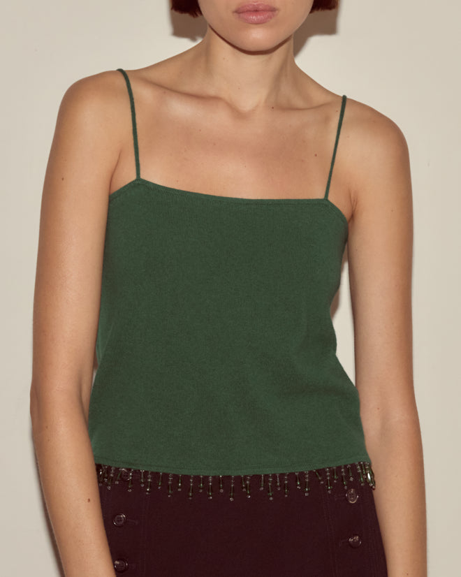 Woman wearing the Lodge Tank in dark green—a cashmere tank with thin straps and a beaded hem—stands against a plain background.