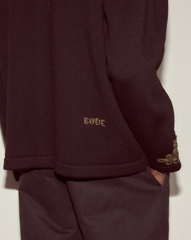 A person wearing the Looped Frog Cardigan, a dark knitwear piece with "BONDE." embroidered above the hem and floral detail on the sleeve cuff.
