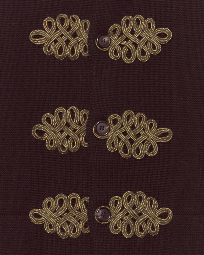 Three dark buttons on fabric with gold ornate braiding beside each, echoing trompe l'oeil frog closures—reminiscent of elegant merino knitwear—adorn the Looped Frog Cardigan.