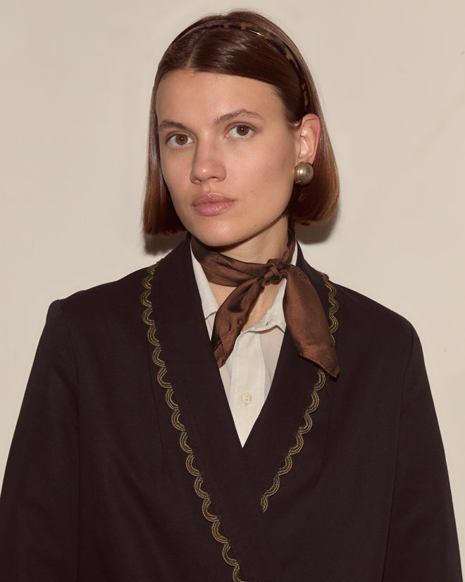 Woman with short brown hair, gold earrings, and headband wears a brown scarf and the Looped Frog Jacket featuring a dark shawl collar, facing forward.