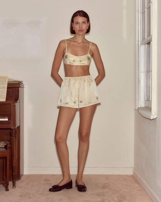 Woman in Lucky Draw Tap Shorts stands indoors by a piano and window, hands behind her back.