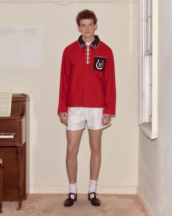 A person wearing the Lucky Horseshoe Pullover, white shorts, and black shoes stands indoors near a piano and window.