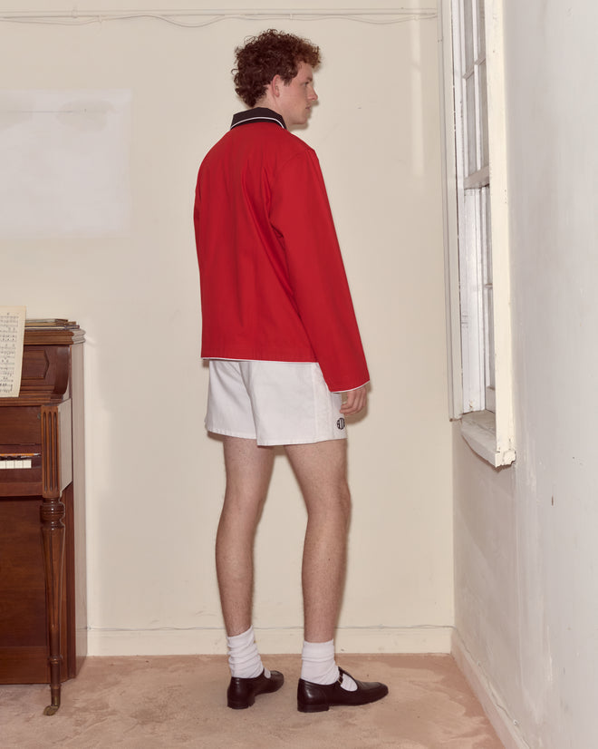 A person wearing the Lucky Horseshoe Pullover and white shorts stands facing a corner of a room beside a window and piano.