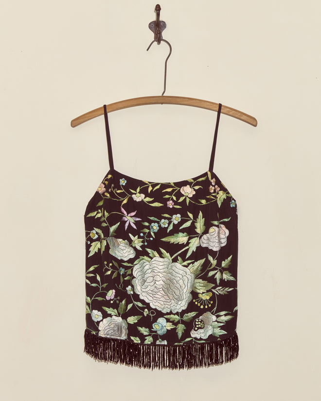 Luna Rose Top - S: Black sleeveless top with floral embroidery and fringe, inspired by an antique piano shawl, displayed on a wooden hanger against a plain wall.