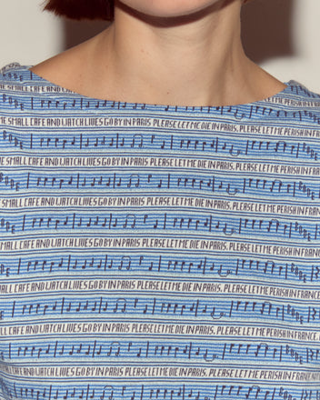 Close-up of the Lyric Long Sleeve in blue, featuring black musical notes, jacquard stripes, and repeated text: 