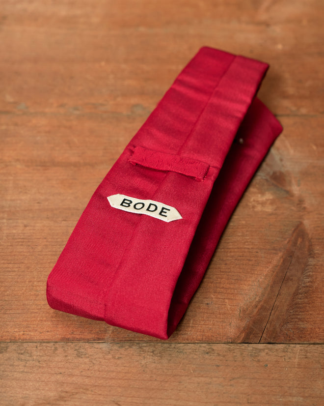 Folded red cotton Luminaire Tie with a label reading “BODE”.