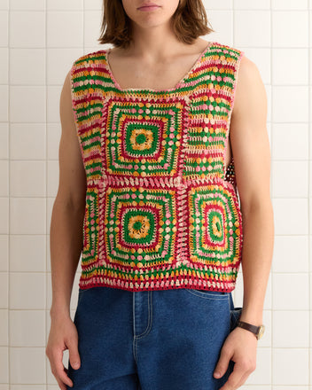 Wearing the Manchester Crochet Tank, hand-crocheted with 100% cotton and featuring vibrant square patterns, a person stands confidently against a tiled wall.