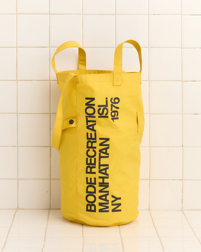 The Manhattan Island Bag is a yellow tote crafted from waxed cotton, adorned with the text 