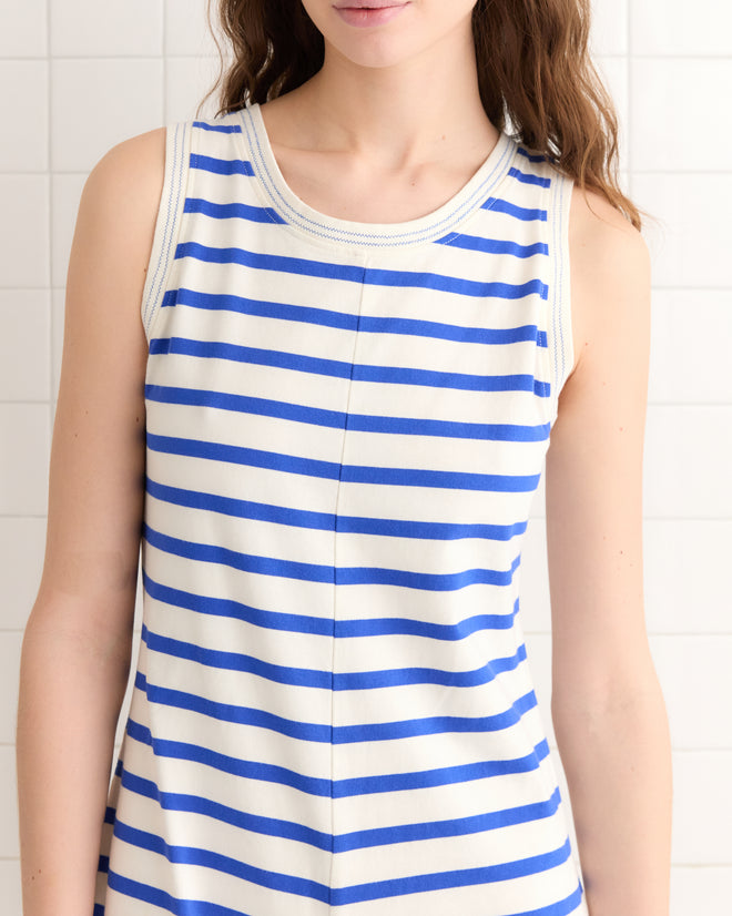 A person wearing the Margate Romper, known for its blue and white stripes inspired by classic French Navy style, stands against a tiled wall.