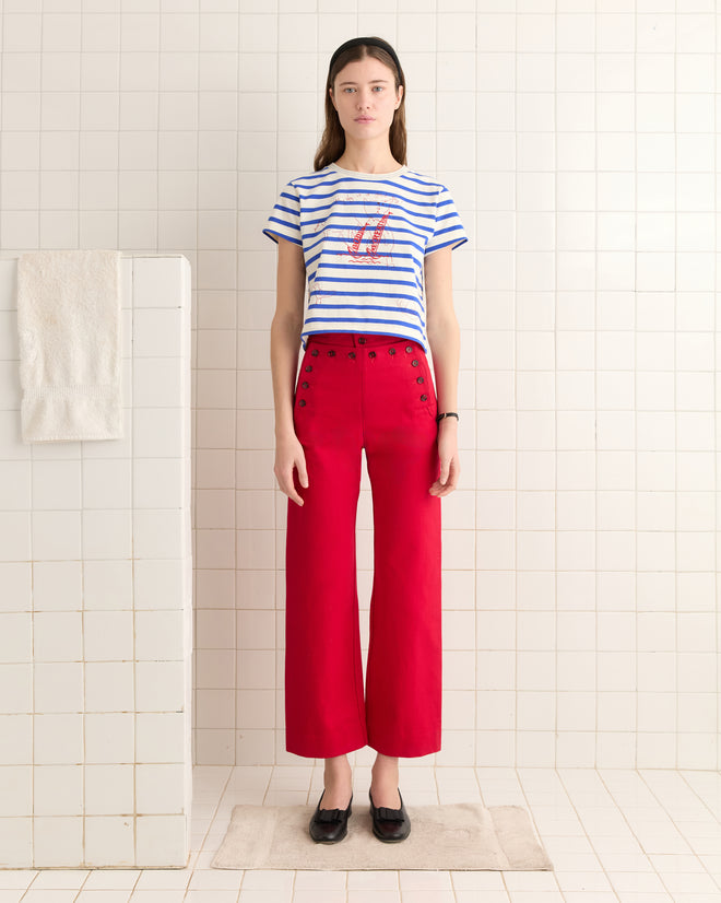 Wearing the Margate Sails Tee and red high-waisted pants, a person stands in a tiled room by a shower, evoking sailor illustration charm.