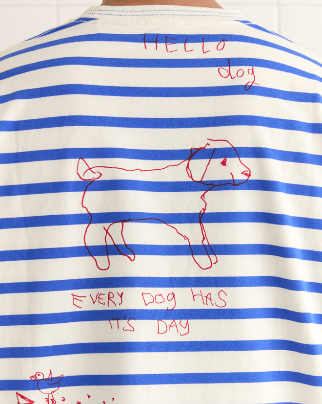 A person wearing a Margate Tee with a French Navy marinière design, adorned with hand-drawn red dog illustrations and the playful text "HELLO dog" and "EVERY DOG HAS ITS DAY.
