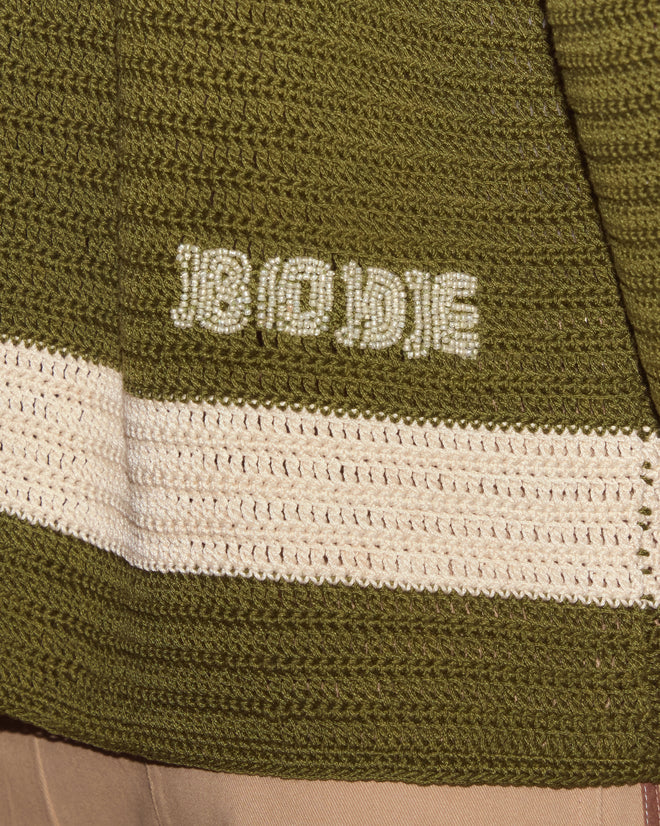 Close-up of the Marsh Crochet Long Sleeve Shirt—hand-crocheted in green cotton with a cream stripe and "BODE" embroidered in cream yarn, highlighting its intricate handmade details.