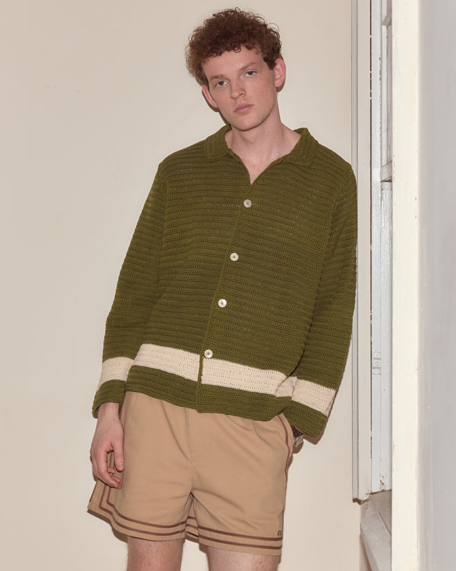 A person wearing the Marsh Crochet Long Sleeve Shirt in green and beige shorts stands by a window, looking at the camera.