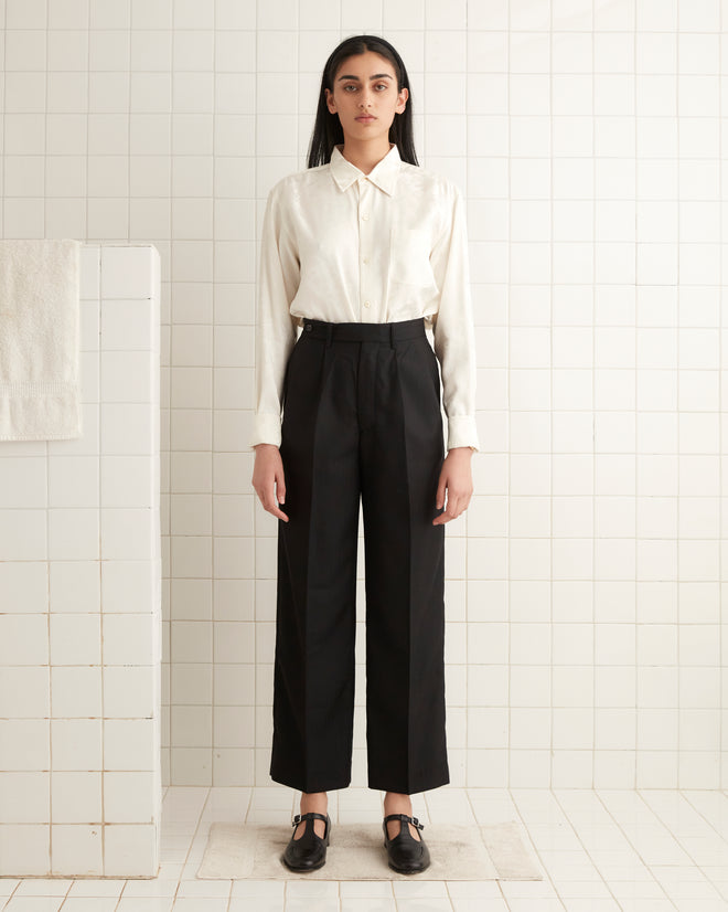 A person in a white shirt and McNab Trousers in black stands in a tiled room with a neutral expression.