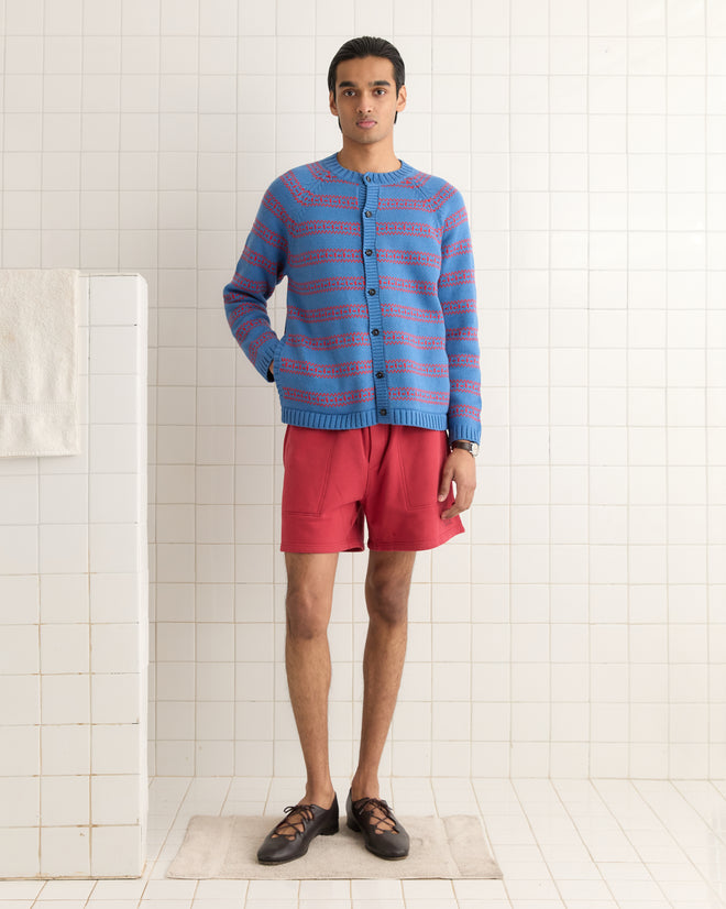 A person in a blue Meandering Stripe Cardigan and red shorts stands on a rug against a tiled wall.