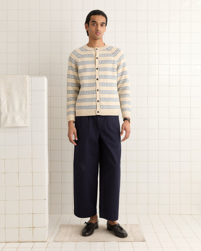 A person in a Meandering Stripe Cardigan - Cream and dark pants stands in a tiled room, with a towel hanging nearby.