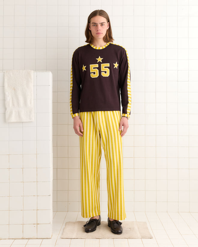 Dressed in a striped Medalist Appliqué Long Sleeve Tee, reminiscent of a vintage basketball jersey with number 55 and star details, a person stands in a bathroom, capturing the 1940s style.