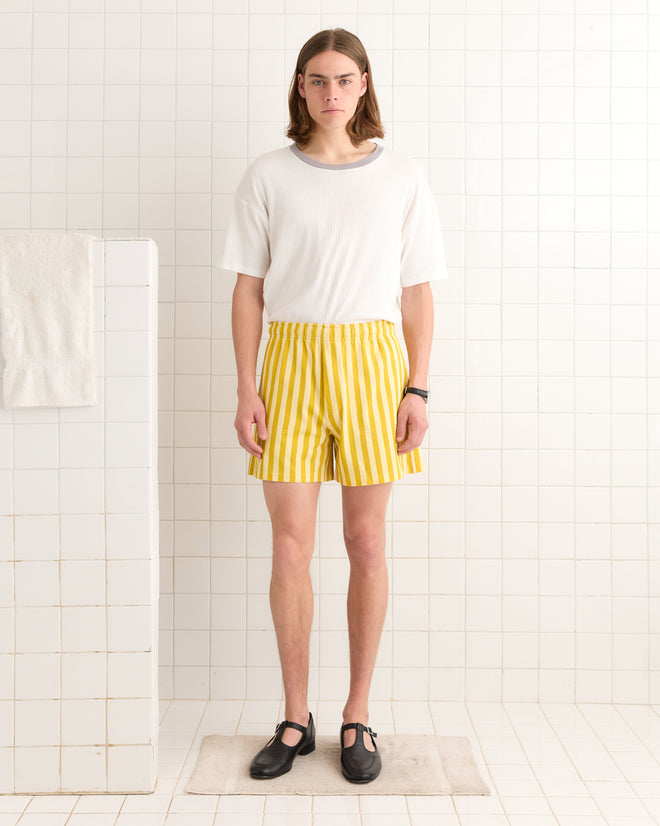 A person wearing a white shirt and Medalist shorts stands in a tiled room with white walls and floor.