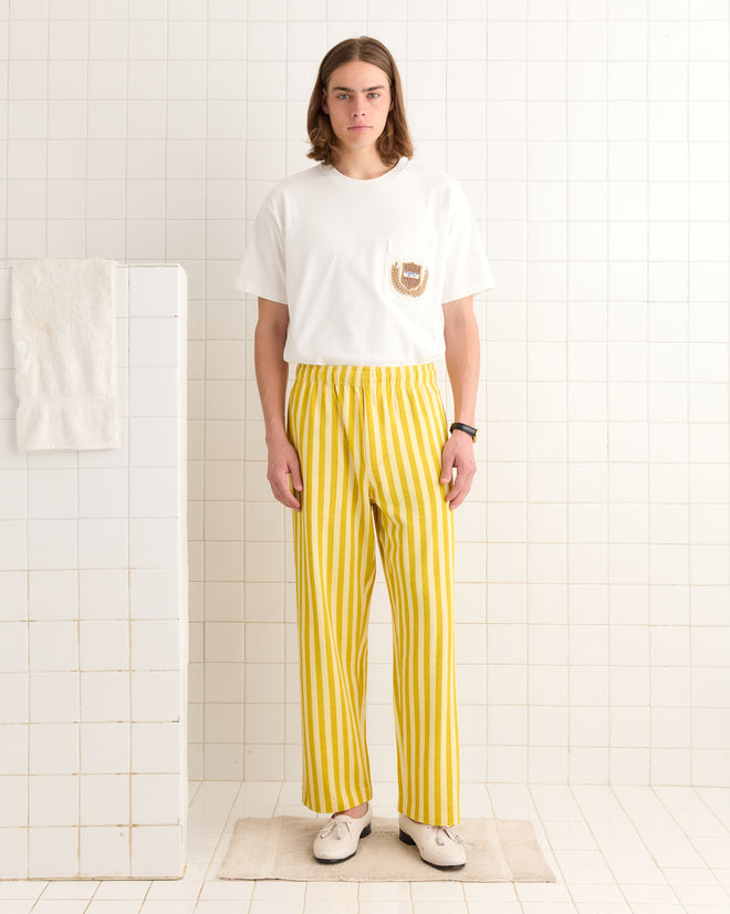A person in a white T-shirt and yellow Medalist Sweatpants stands in a white tiled room.