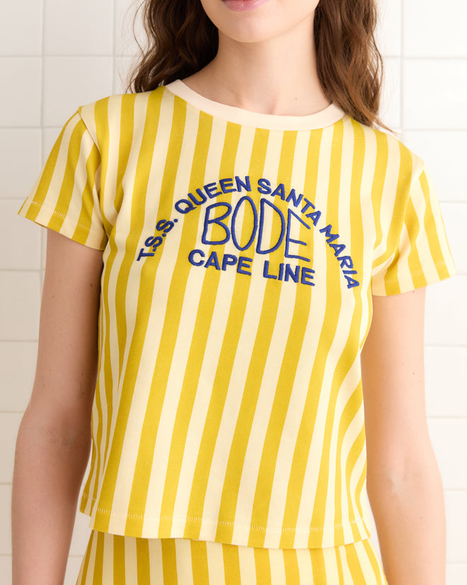 A person proudly wears the Medalist Tee, showcasing its vintage charm with yellow and white stripes and the "T.S.S. QUEEN SANTA MARIA BODE CAPE LINE" text, reminiscent of classic cruise line shirts.