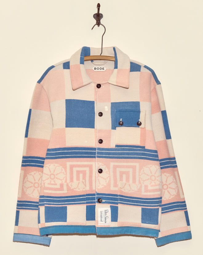 A pastel pink, blue, and cream Medallion Checker Jacket - S/M by BODE with geometric patterns hangs on a wall hook.
