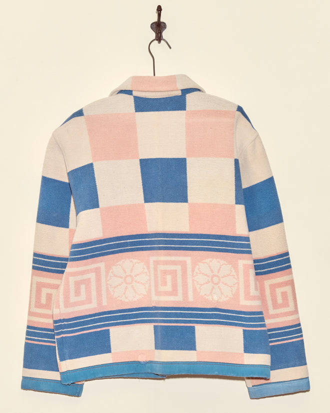 The Medallion Checker Jacket - S/M features a unique blue, pink, and white checkerboard pattern with a Greek key design, crafted from midcentury wool and displayed hanging on a hook.