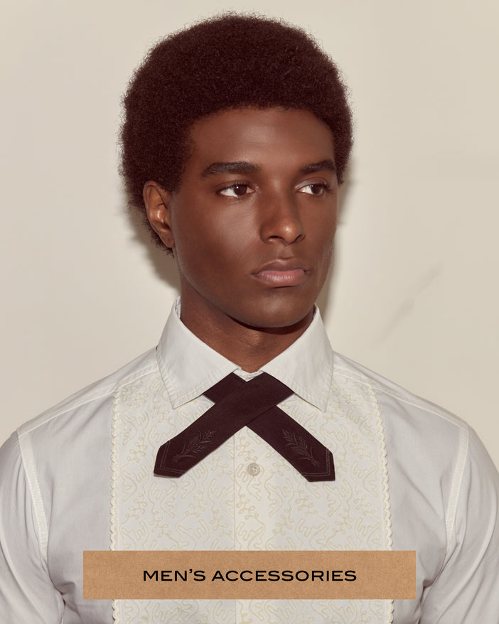 Portrait of a model wearing a tuxedo shirt and a black cross tie with embroidered details on it.